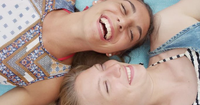 Top view of teenage girl friends lying on back smiling laughing at beach direct from above