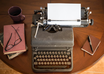 black vintage typewriter sitting on brown wooden table next to brown leather notepad and pen, and...