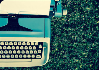 old vintage typewriter sitting outside in a beautiful garden underneath a tree. This equipment sits...