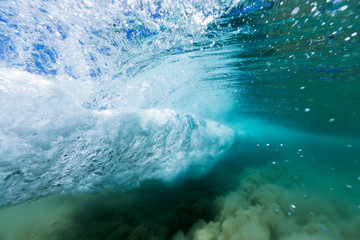 A breaking wave forms a vortex in crystal clear ocean water in this underwater image.