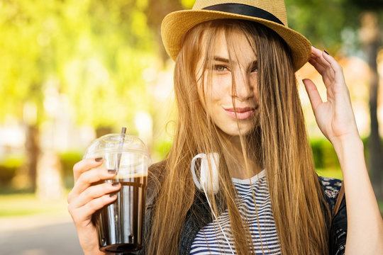 Young teenage millennial girl in hat, holding takeaway coffee in park