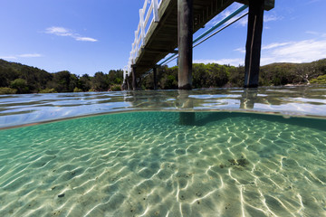 A bridge crosses over beautiful pristine water on a summer day in this underwater split image.
