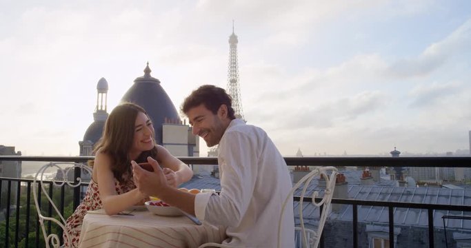 Romantic couple in Paris using technology digital tablet smart phone taking photo hotel breakfast terrace honeymoon Eiffel Tower Paris destination 