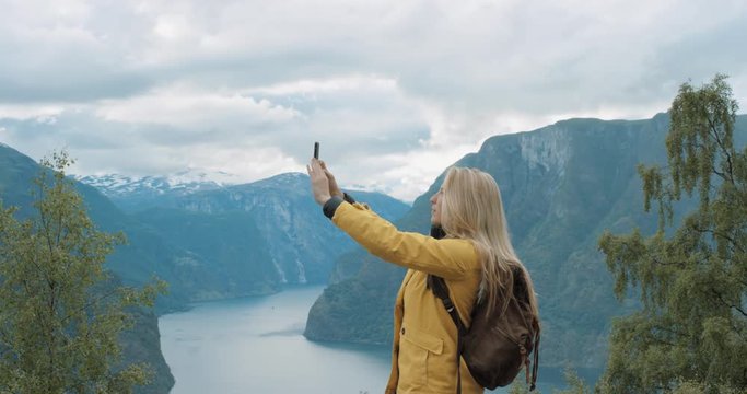 Woman taking panorama photograph fjords with smartphone photographing scenic landscape from high up nature background view enjoying Norway vacation travel adventure