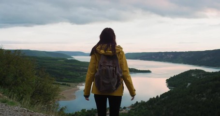 Beautiful woman arms raised enjoying sunset landscape travel adventure celebrating nature wearing yellow jacket