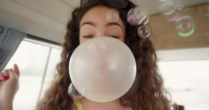 Portrait Beautiful African American Teenage girl blowing bubblegum candy bubbles having fun at festival in camper van on road trip adventure