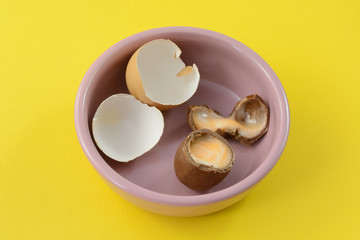 Broken Easter chocolate cream egg with broken eggshells in pink dish against yellow background