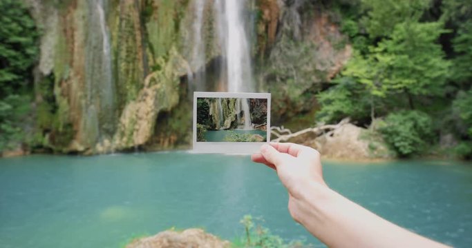 Hand holding instant photo in front of waterfall travel concept