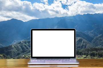Front view of laptop computer with blank screen on wooden table with mountain, cloudy and sky background.