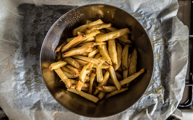Silver cooking bowl full of homemade potato fries straight out of the oven, placed on baking tray