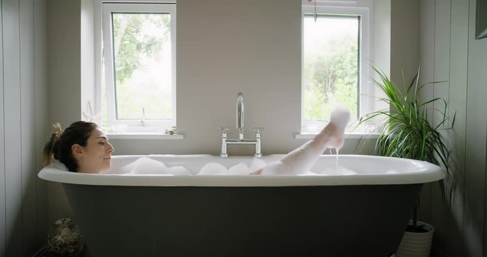 Beautiful Woman lying in bathtub enjoying relaxing bubble bath experiencing mindfulness lifestyle with real natural body care authentic homemade spa treatment