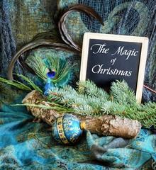 BOHO style Christmas image with log, greenery, fabric and ornaments in rich, dark teal tones with Christmas message on a blackboard