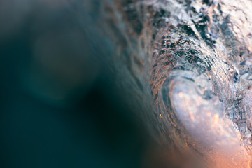 Abstract, close up water shot of the inside of a breaking, barrelling wave as golden sunset light...