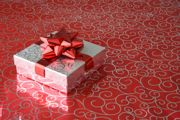 Silver wrapped Christms present or Valentines gift with red bow and ribbon on metallic red wrapping paper - Powered by Adobe