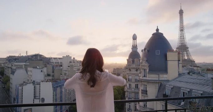 Young tourist woman stretching in morning on hotel balcony with view of Eiffel Tower Paris arms raised enjoying european travel adventure celebrating beautiful city sightseeing exploration