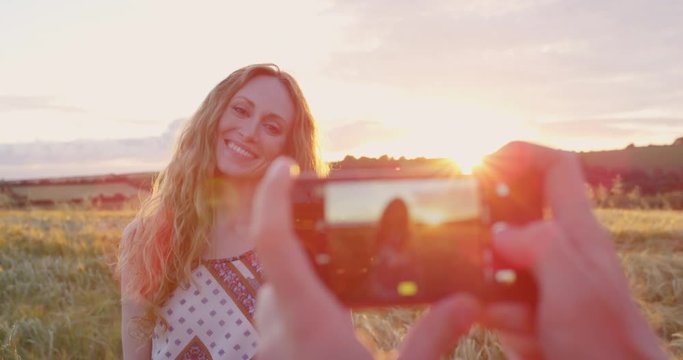 Tourist taking photograph of beautiful woman at sunset in open field in nature
