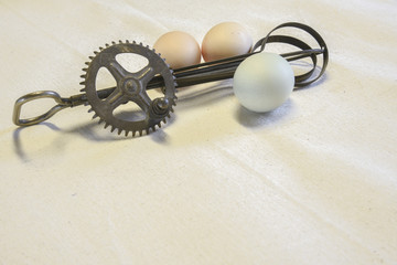 Clolorful, organic, free range chicken eggs with an antique manual beater on a cloth surface