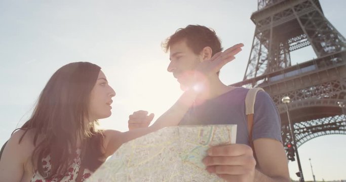 Tourist couple reading City Map under Eiffel Tower planning European holiday In Paris Summer Vacation having disagreement fighting over directions