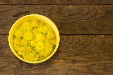 A bowl of dandelion flowers on a rustic wood background with room for text.