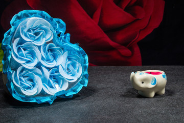 A box with buds of blue roses and a candle-elephant on a dark background