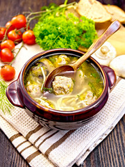 Soup with meatballs and spoon in clay bowl on dark board
