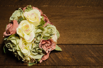 A pink, white and green silk floral bouquet of roses on a rustic wood background with copy space