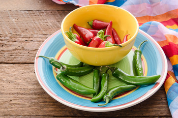 Cinco De Mayo background with green serrano and red fresno peppers and a bright striped fabric on dark wood