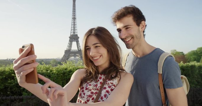 Beautiful tourist couple taking selfie using smartphone in Paris on Honeymoon enjoying European summer holiday travel vacation adventure