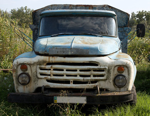 Old truck with a blue and white painted cabin abandoned in the grass