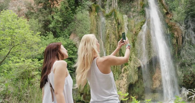 Girl friends taking photograph of secret waterfall with smartphone photographing scenic landscape nature background view enjoying vacation travel adventure