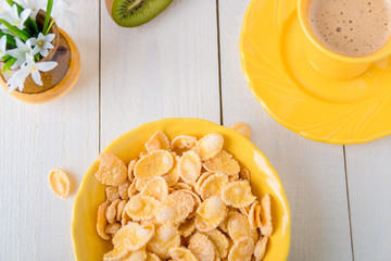 Healthy breakfast with cereal flakes  near vase with flowers on white background. Yellow tone. Top view