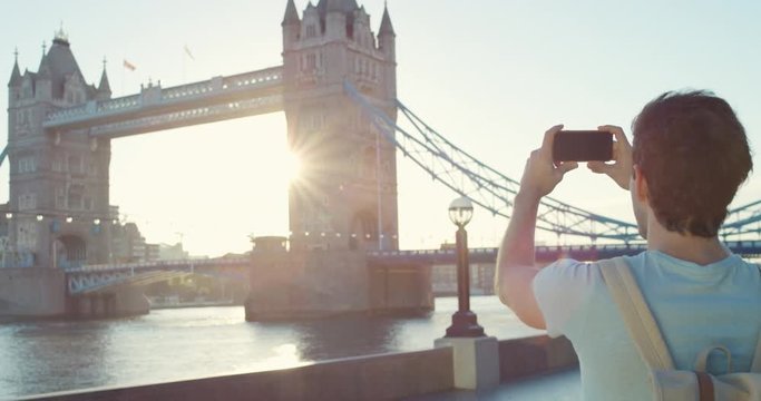 Man taking photograph in city at sunrise smartphone photographing Tower bridge London enjoying Europe vacation travel adventure