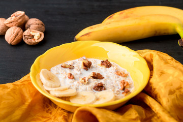 Oatmeal with walnuts and banana in yellow bowl on black background.. Healthy breakfast