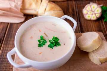 Cream soup in white bowl near bread on wooden background. Rustic style.
