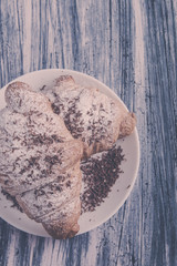 Croissants with powdered sugar and chocolate on white plate on colored wood background. Top view. Copy space