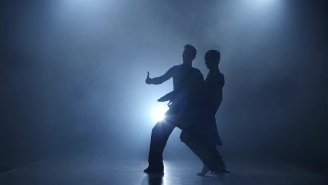 Dance tango performed by professional couple in smoky studio, silhouette