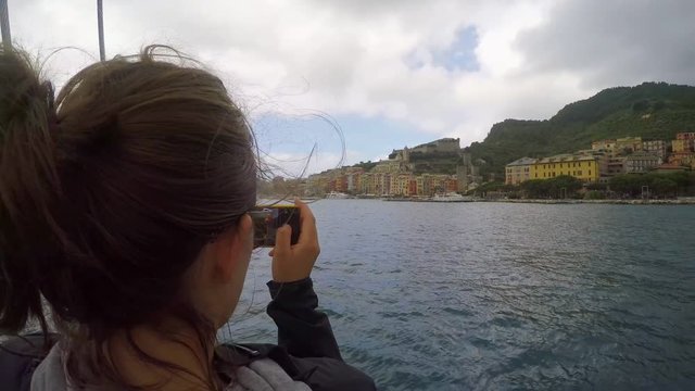 Travel woman taking photos of Italy coast with smart phone technology from luxury sailboat for social media sharing 