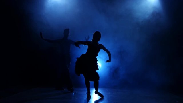 Silhouette of pair dancers performing modern dance in smoky studio