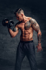 Fototapeta na wymiar Athletic male with tattoo on his chest doing biceps workouts with dumbbell.