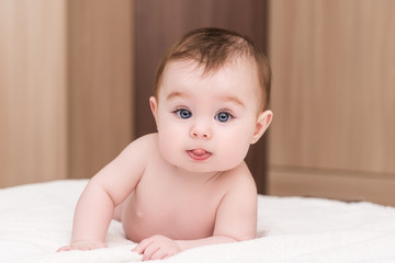 adorable baby girl lying on her stomach on soft blancket and show tongue. portrait of cute baby girl with blue eyes and long eyelashes © IrBreeze
