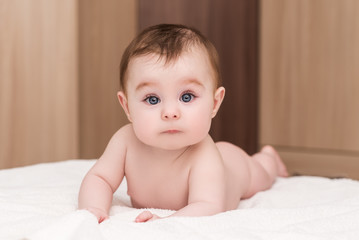 portrait of adorable baby girl with big blue eyes and long eyelashes. cute baby lying on her stomach on soft blanket and looks into a camera with surprised © IrBreeze