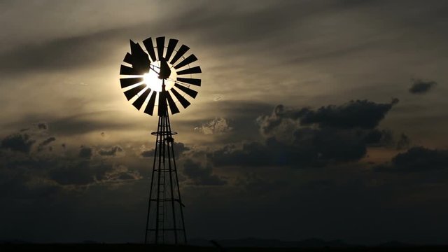 A windmill turning in the wind against a setting sun and storm clouds