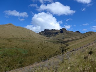 Blue sky, puffy white clouds and open grass land on a beautiful hiking trail in Ecuador. 