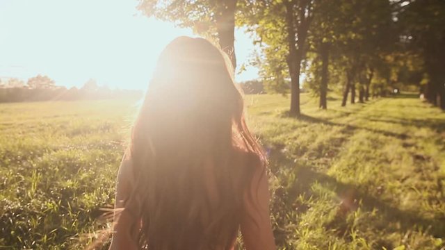 Beautiful girl with long hair goes on a green trail among the trees, circling and enjoying the sun and nature.