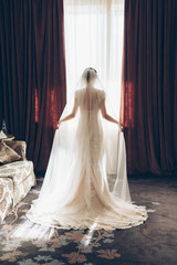 silhouette of the bride standing at the window and holds the curtain