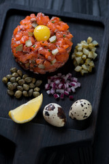 Close-up of salmon tartar served with quail egg yolk, lemon, chopped capers, red onion and pickles, selective focus