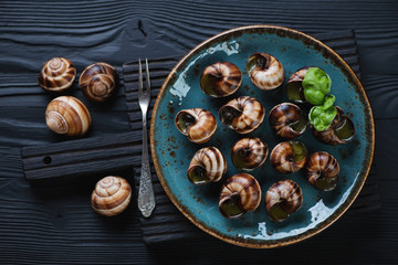 Above view of baked bourgogne snails with garlic butter over black wooden background