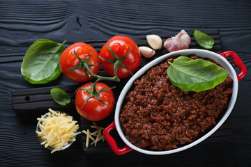 Freshly made bolognese sauce with green basil leaves, ripe tomatoes, garlic and parmesan over black wooden background
