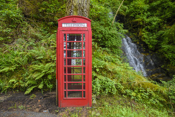 Red telephone box in the forest next to a waterfall