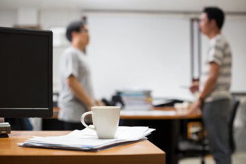 Close up coffee cup on paperwork table with blurry business men discussing.